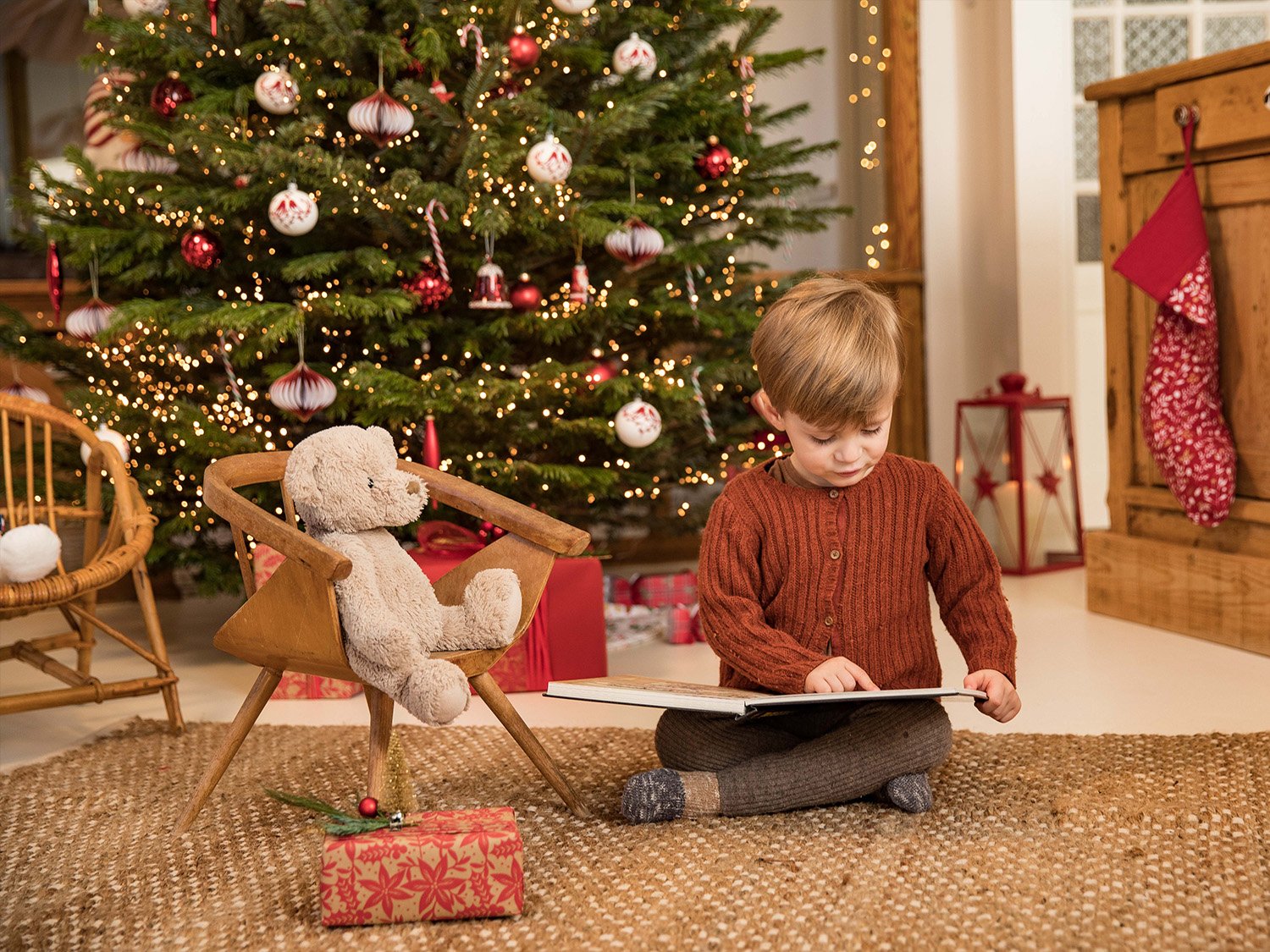 Enfant devant un sapin de Noël en train de lire un livre