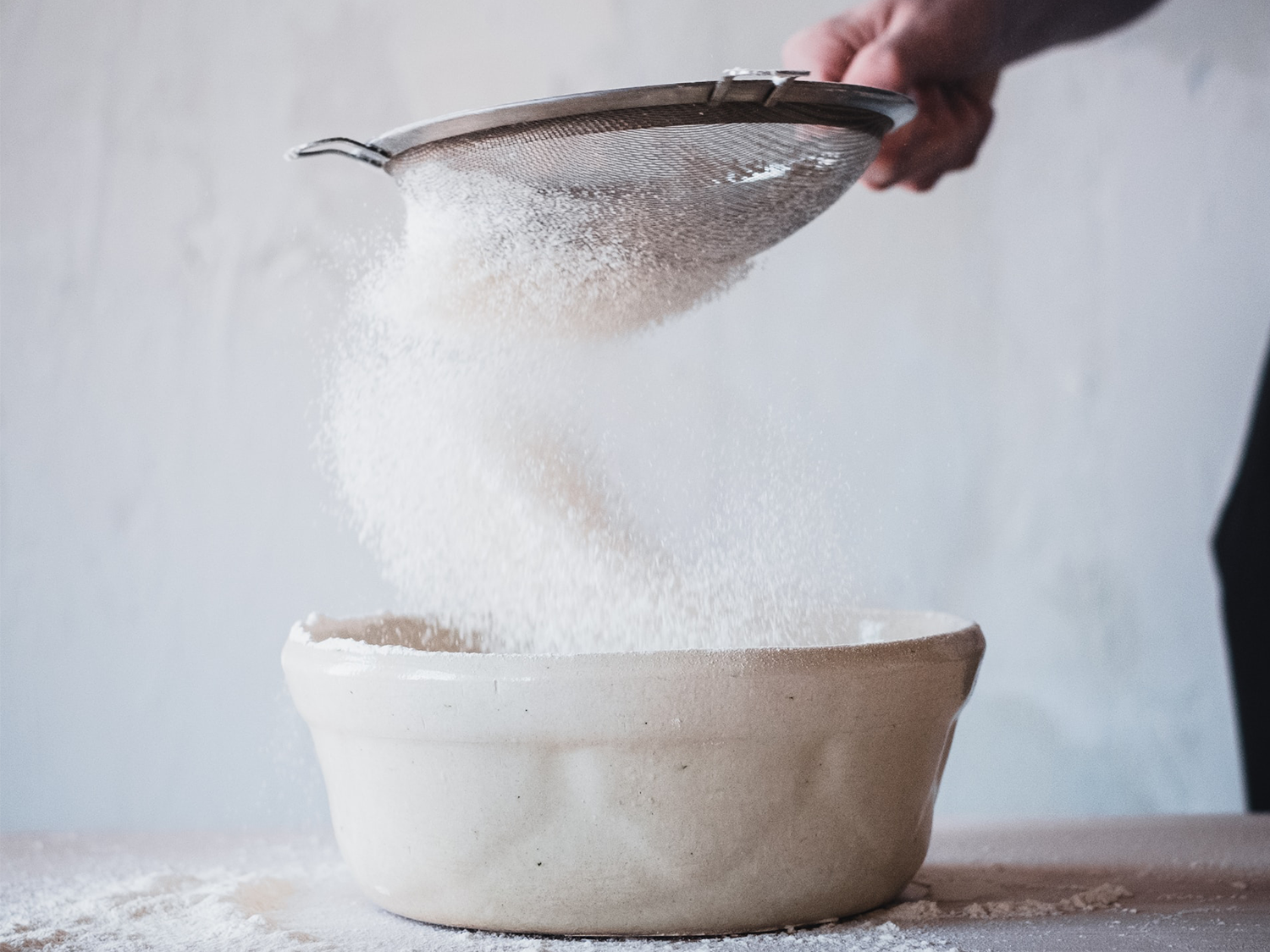 Une personne tamise du sucre dans un bol