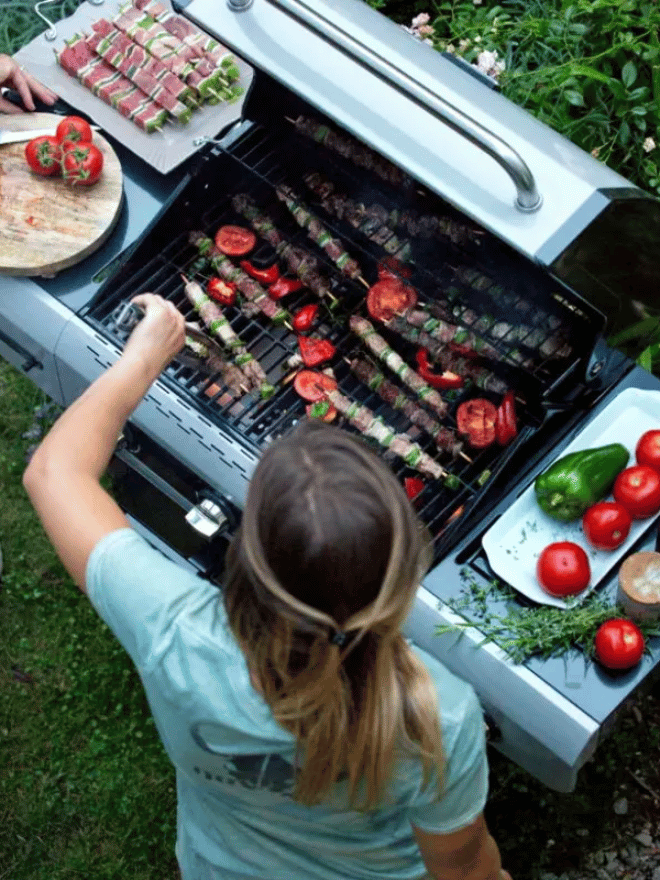 Une femme en train de déposer une brochette sur un barbecue