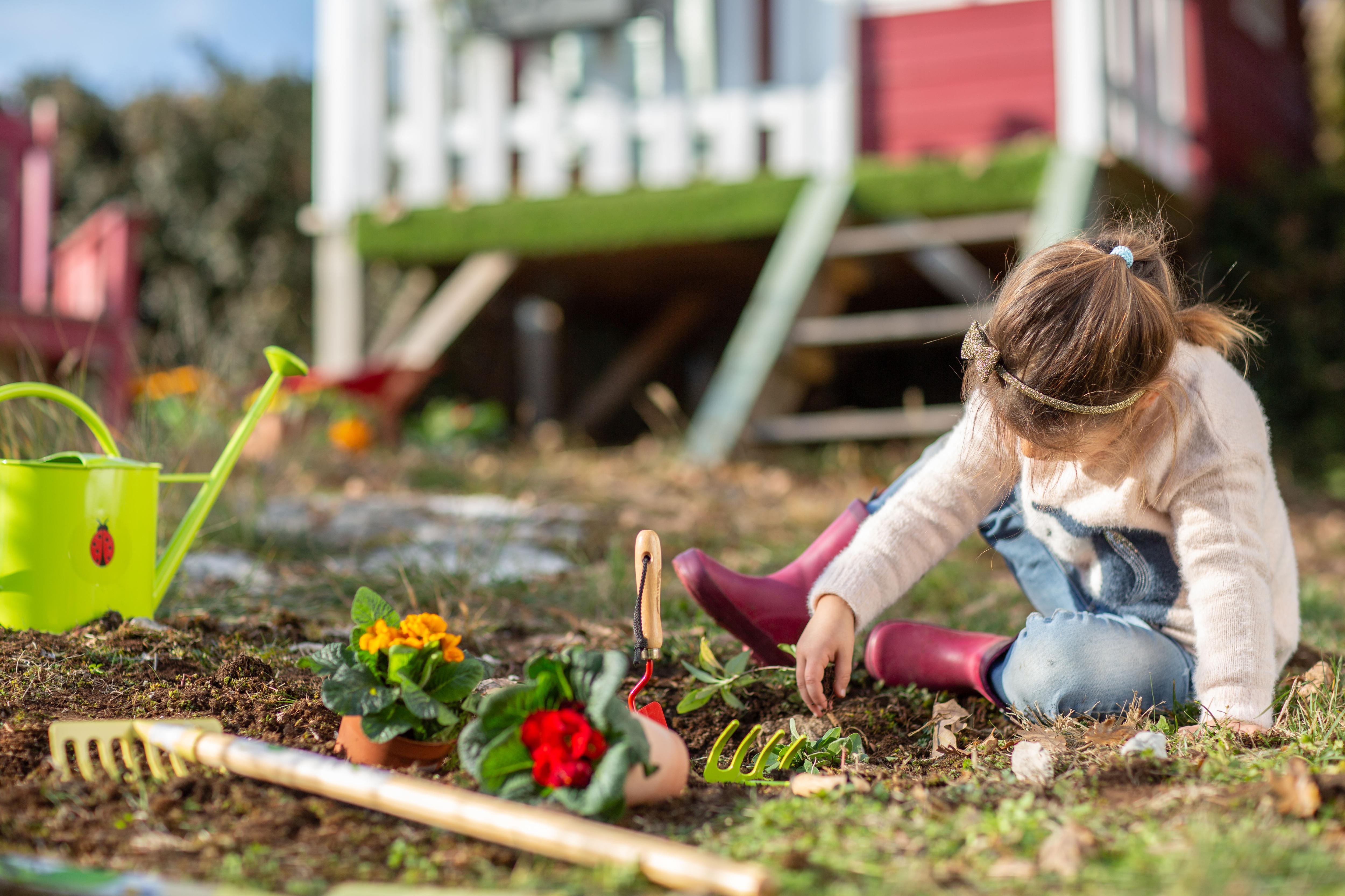 Une petite fille qui joue avec un râteau et un arrosoir dans un jardin