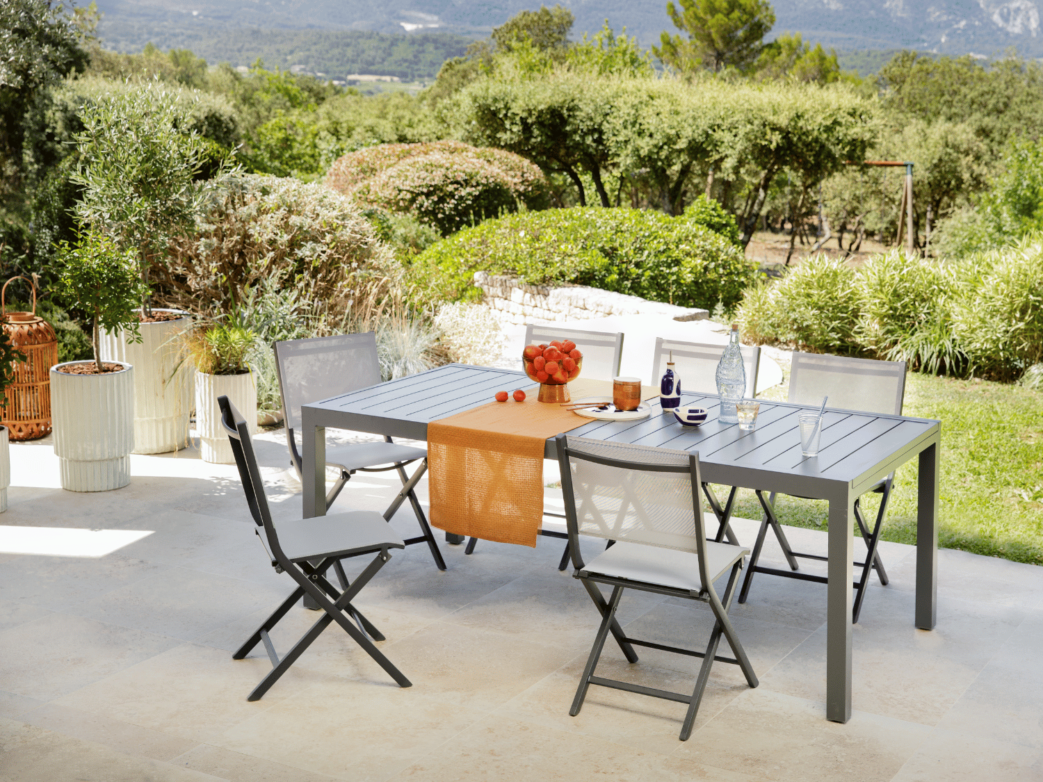 Une table Zinna exposée sur une terrasse dans un jardin avec des arbustes et des haies