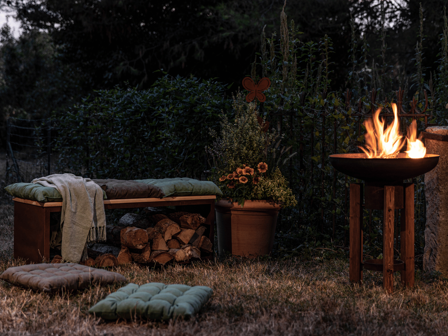 Un brasero allumé dans le jardin avec un banc et des coussins d'extérieur