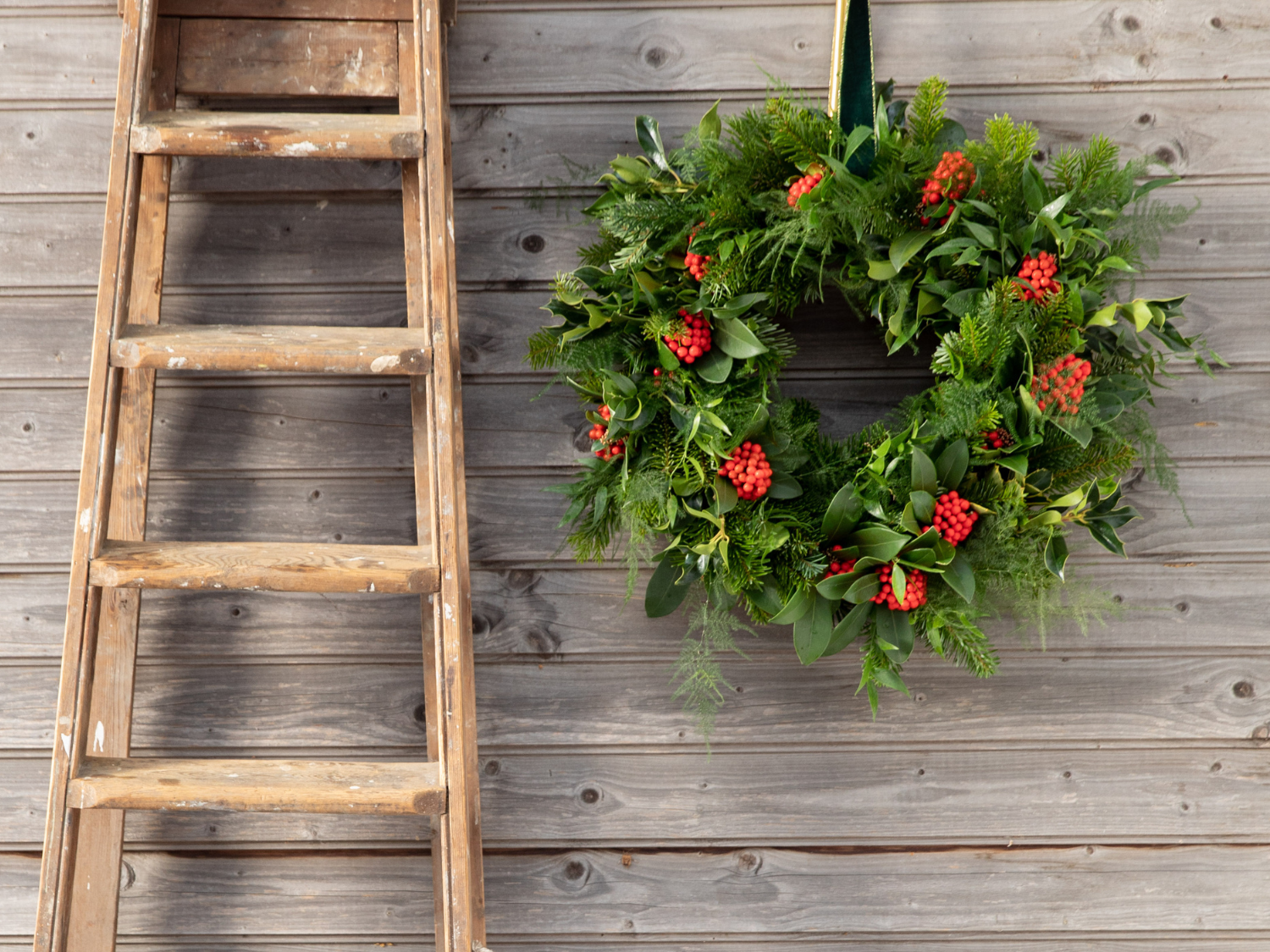 Une couronne de noël à côté d'une échelle en bois contre un mur