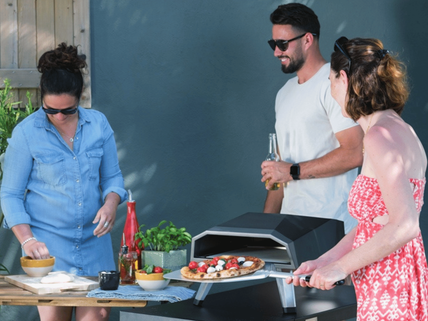 Trois personne devant un four a pizza avecc des bières à la