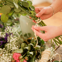 Une femme enroule une ficelle autour de tiges de fleur.