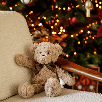 Un ours en peluche assis sur un fauteuil devant le sapin de Noël