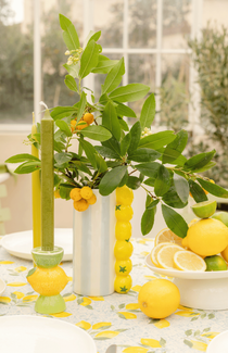 Une table colorée sur le thème des agrumes avec un vase rempli de branche de kumquat et des citrons sur un plateau