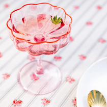 La coupette de champagne Fleur avec du vin rosé dedans posée sur une nappe au motif fleuri