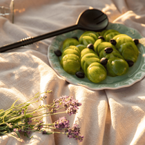 Une salade de tomates vertes dans une assiette avec une pince posés sur une nappe avec un brin de lavande