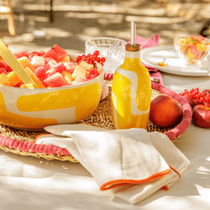 Une salade de fruits colorées avec de la pastèque, des framboises et groseilles posée sur une table avec un huilier et un torchon