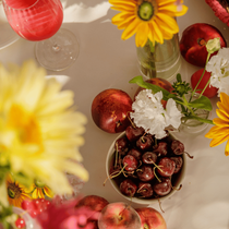 Des cerises dans une coupe sur une table où il y a des fleurs et des pêches