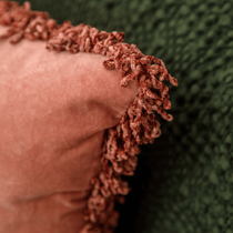Zoom sur un coussin rose posé sur un plaid vert sapin