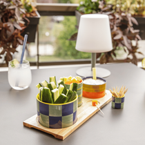 Une lampe solaire nomade posée sur une table de jardin à côté d'apéritifs