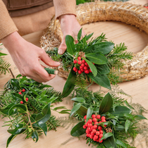 Une femme qui fabrique une couronne de noel avec des branches de sapin et de houx