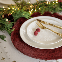 De la vaiselle de Noël blanche et or avec un set de table bordeaux