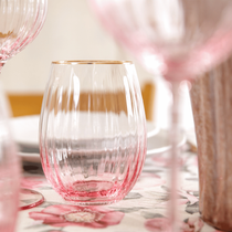 Le verre à eau Gatsby posé sur une table de couleur rose et transparent et orné d'un liseret doré