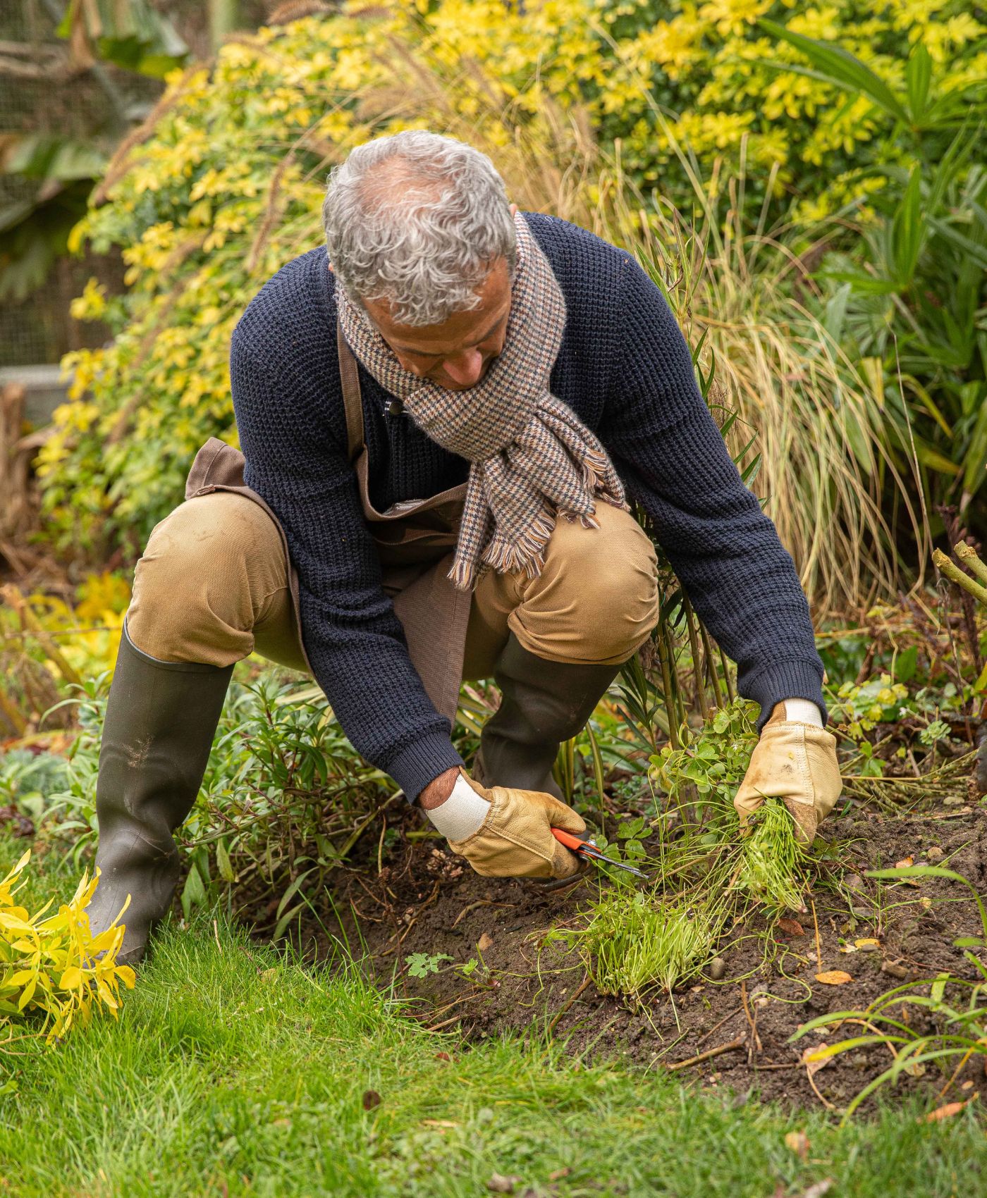 Un homme ayant des ciseaux de jardinage à la main qui est accroupi en train de couper des mauvaises herbes