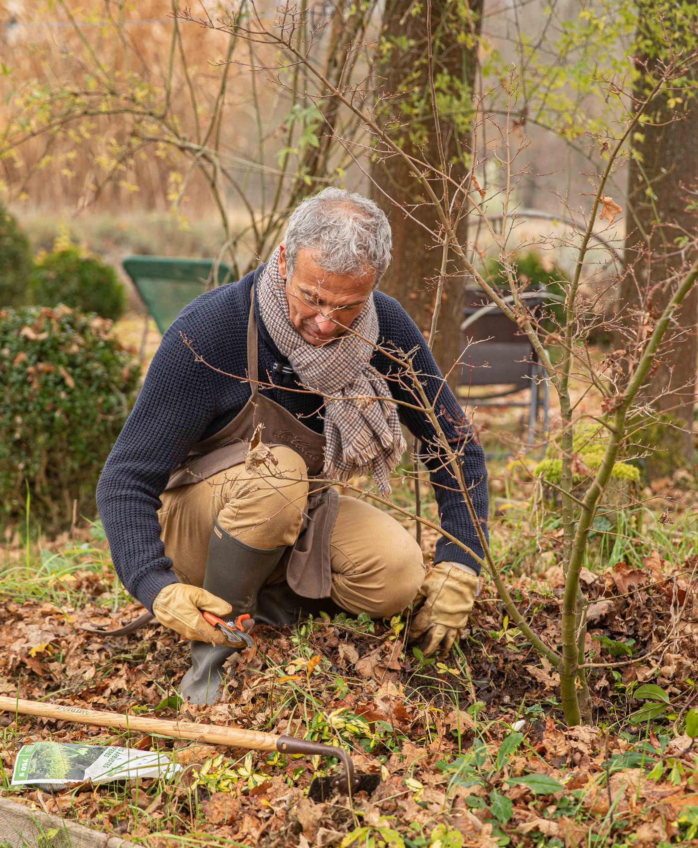 Un homme qui est accroupi dans son jardin potager en train de prendre des ciseaux de jardin pour couper les mauvaises herbes