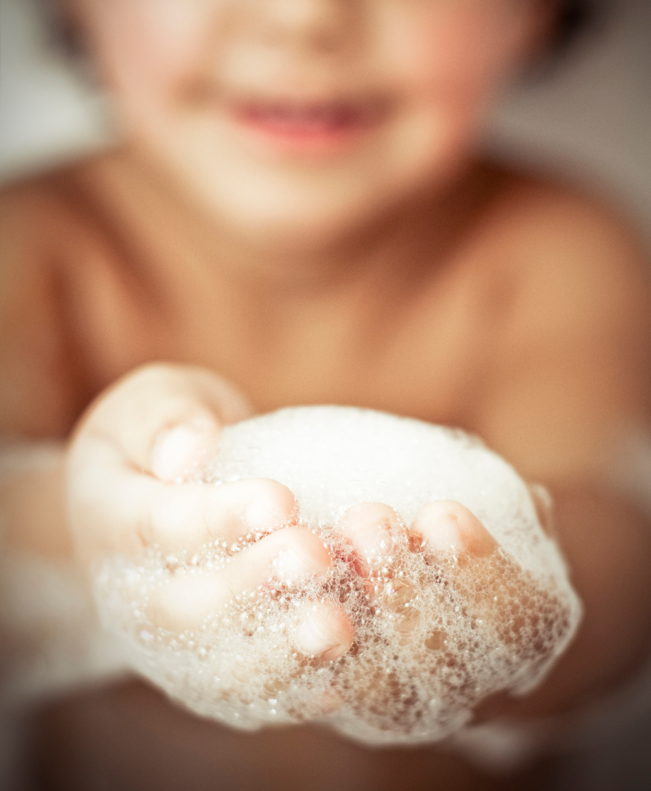 Un enfant qui montre la mousse de son bain entre les mains