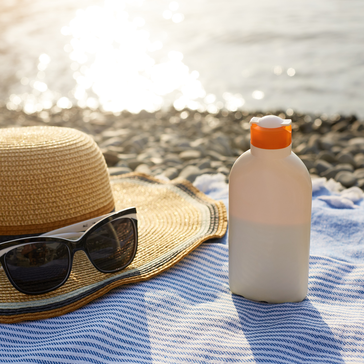 Un chapeau, des lunette de soleil et une crème solaire sur une serviette face à la mer