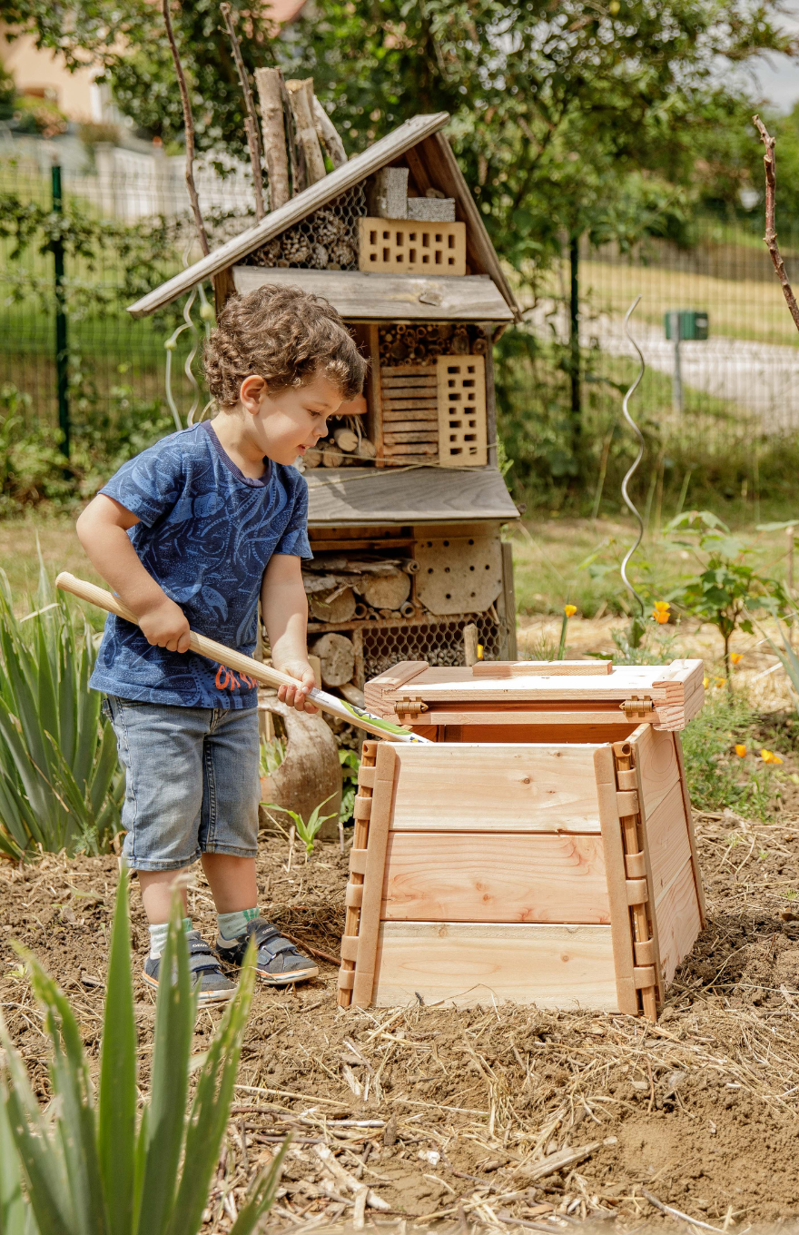 Un enfant utilise un composteur en bois dans son jardin