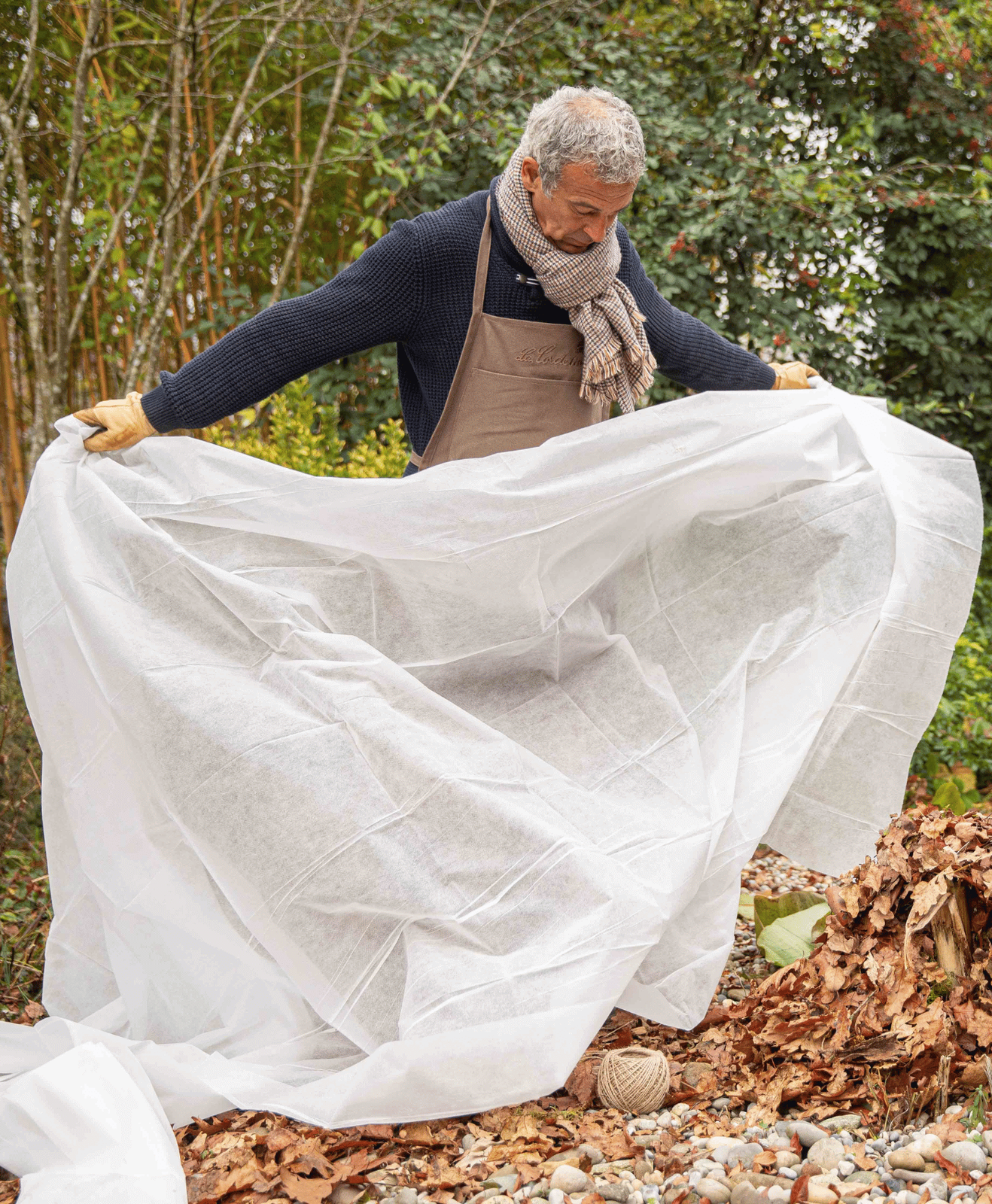 Visuel d'un homme qui couvre une plante avec un voile d'hivernage