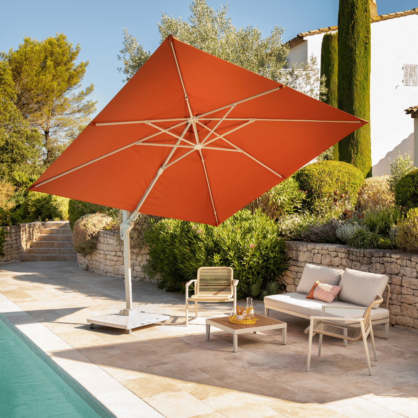Un parasol orange qui fait de l'ombre à un salon de jardin au bord de la piscine