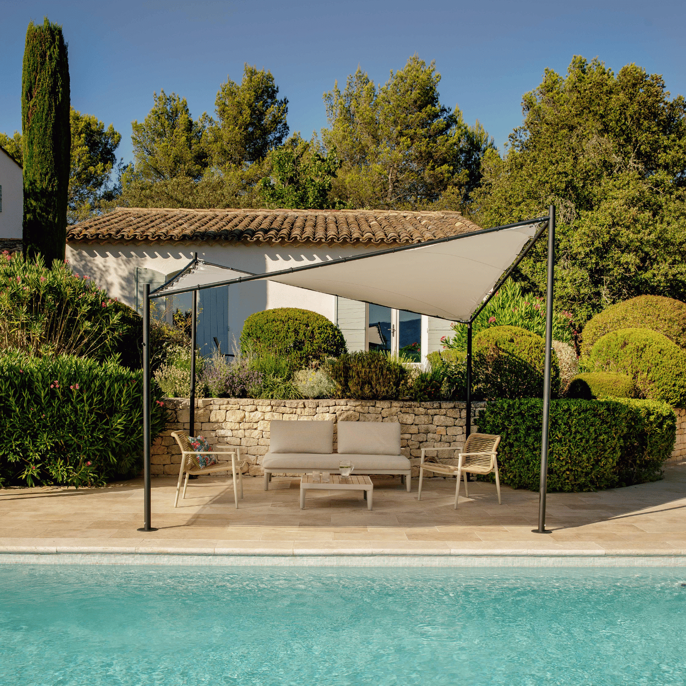 Une tonnelle qui fait de l'ombre à un salon de jardin au bord de la piscine