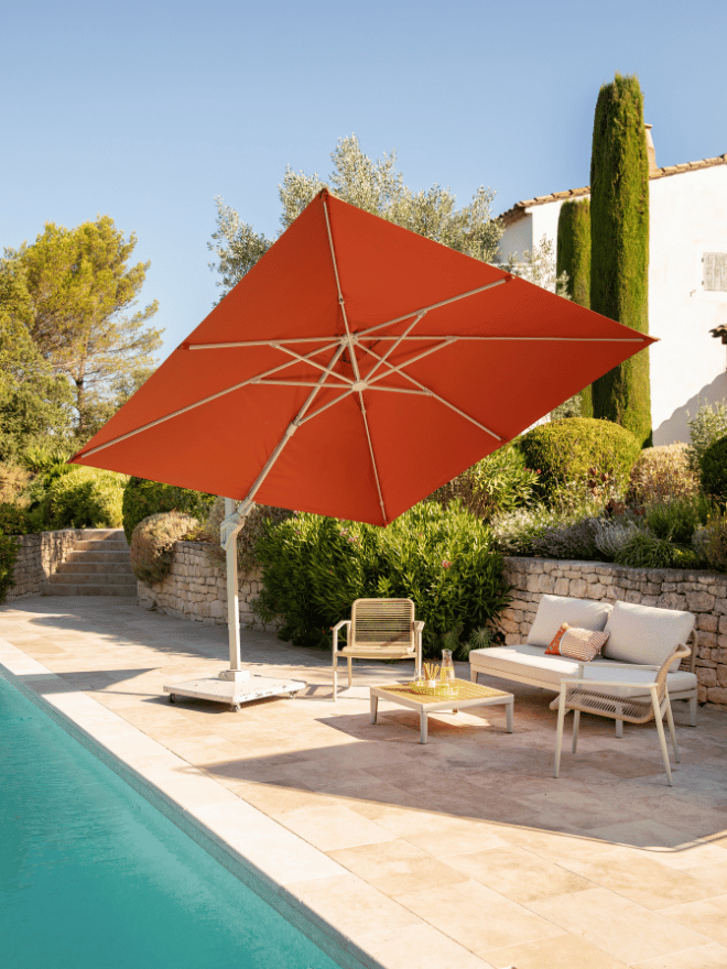 Un parasol orange qui fait de l'ombre à un salon de jardin au bord de la piscine