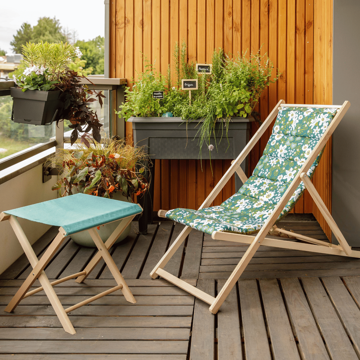 Une chilienne fleurie et un tabouret vert installés sur un balcon, entourés de plantes.