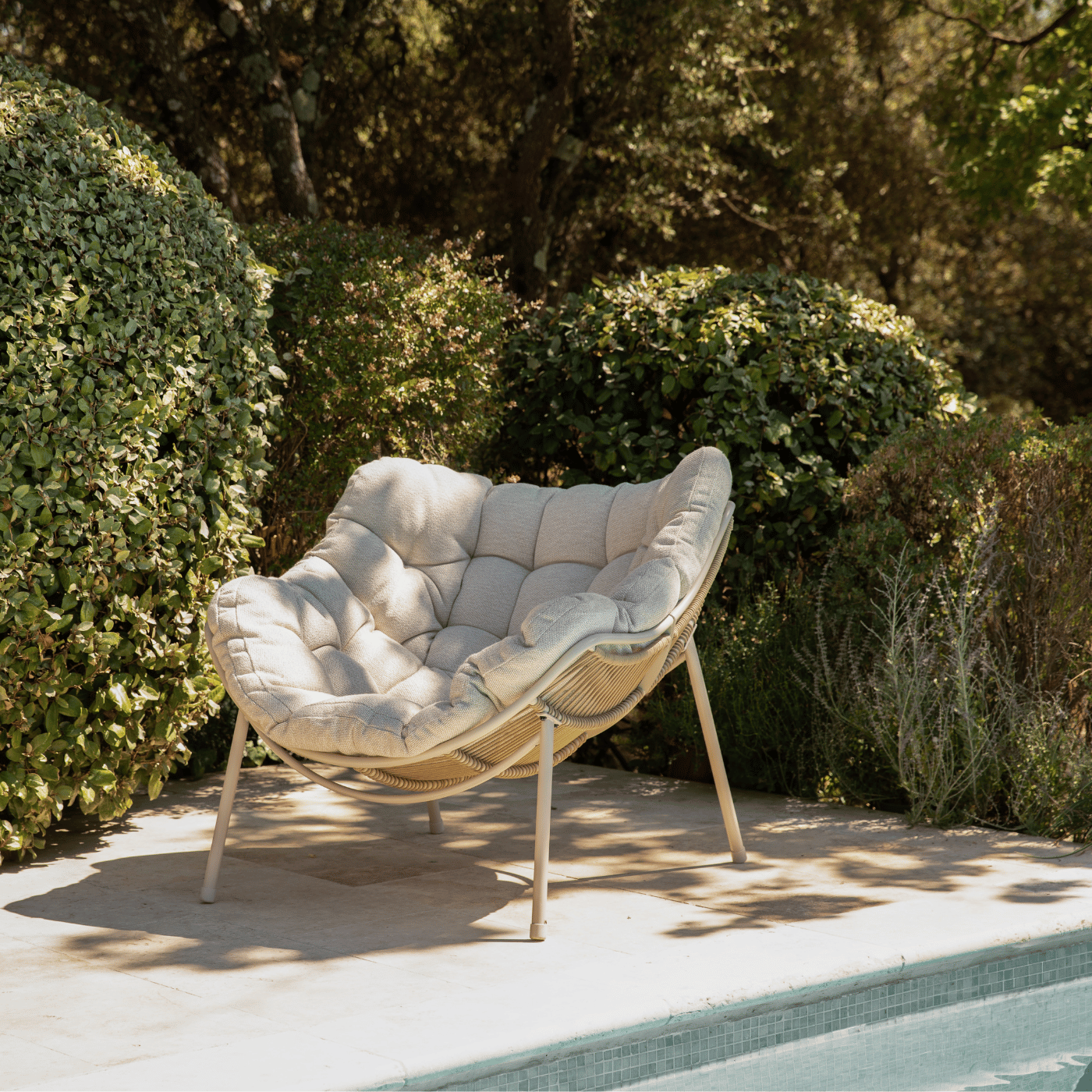 Un fauteuil relaxant beige sur une terrasse, au bord de la piscine, entouré de verdure.