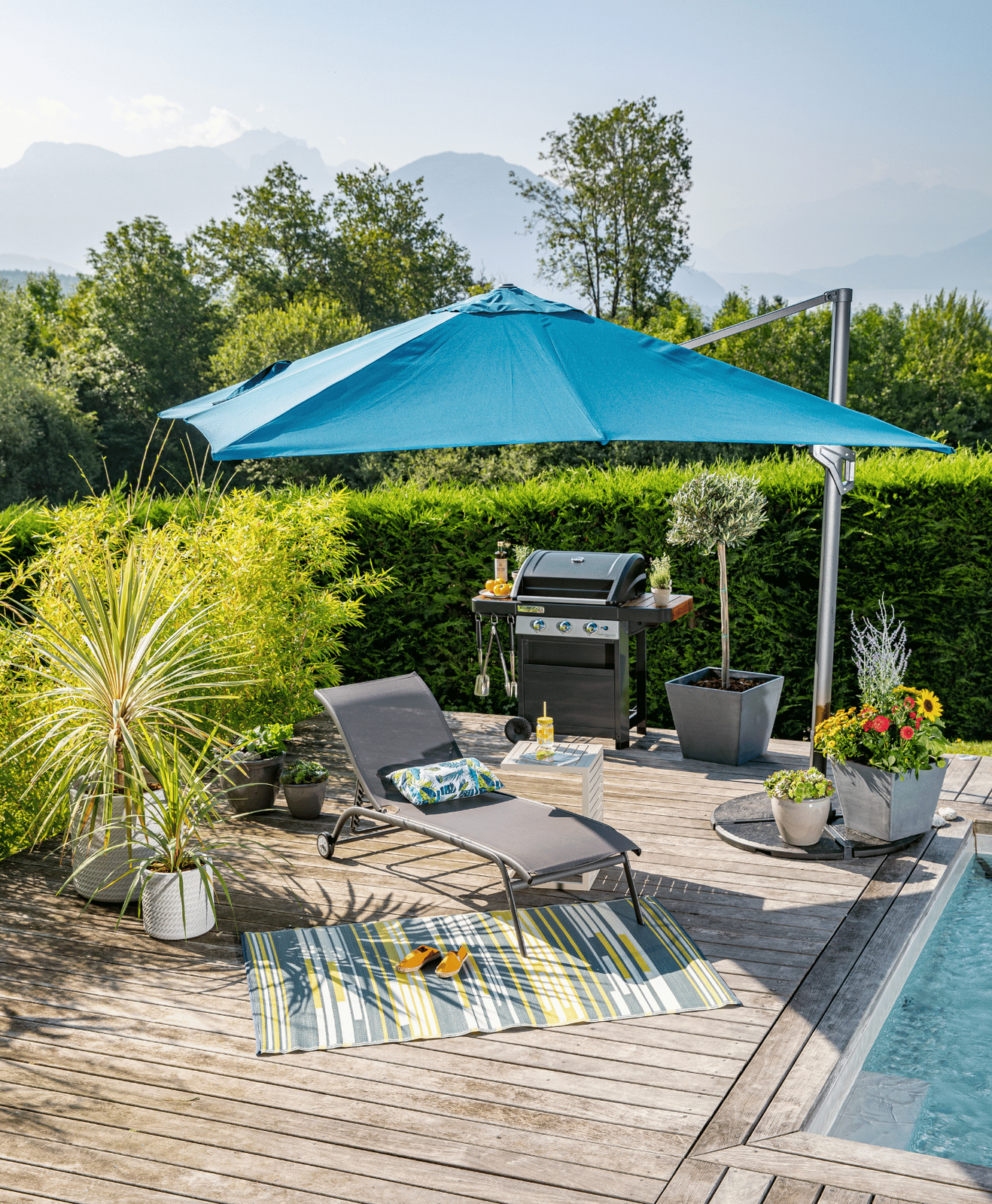Une terrasse aménagée avec un bain de soleil, un parasol, des pots, des végétaux et un tapis