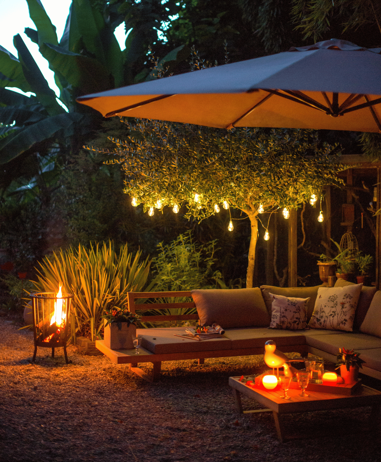 Une terrasse extérieure aménagée avec un brasero, un parasol, un salon de jardin et des guirlandes