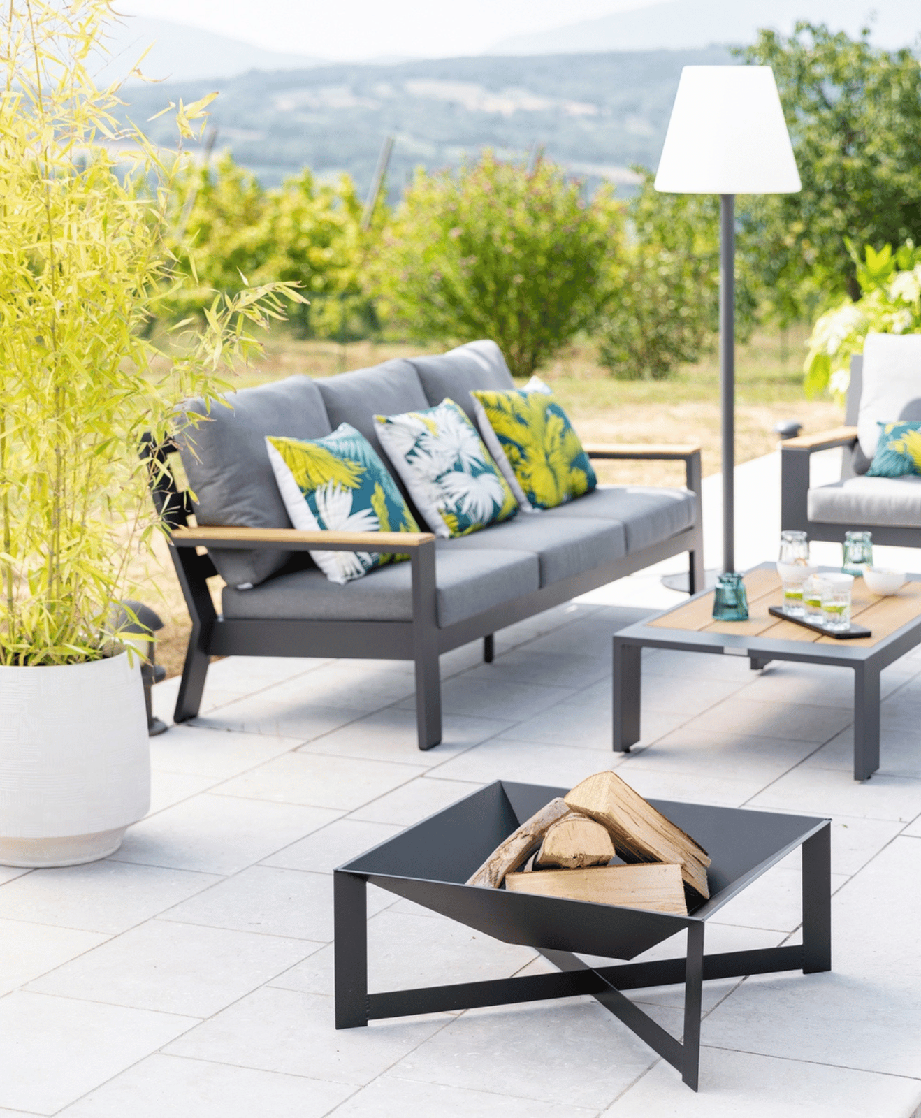 Un brasero sur une terrasse avec un salon bas, des coussins et une lampe