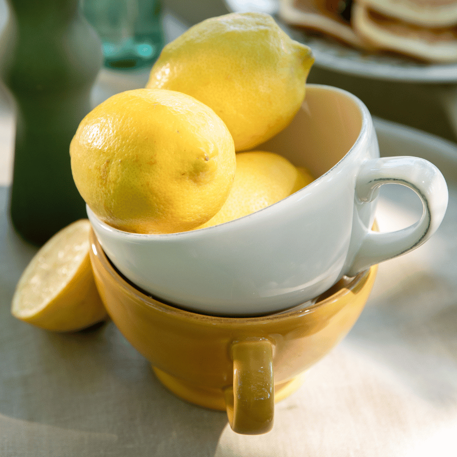 Une tasse jaune et une tasse blanche empilées avec des citrons jaunes a l'intérieur.