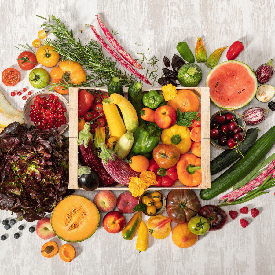 Cagette de fruits et légumes variés entourée de produits frais d’été.
