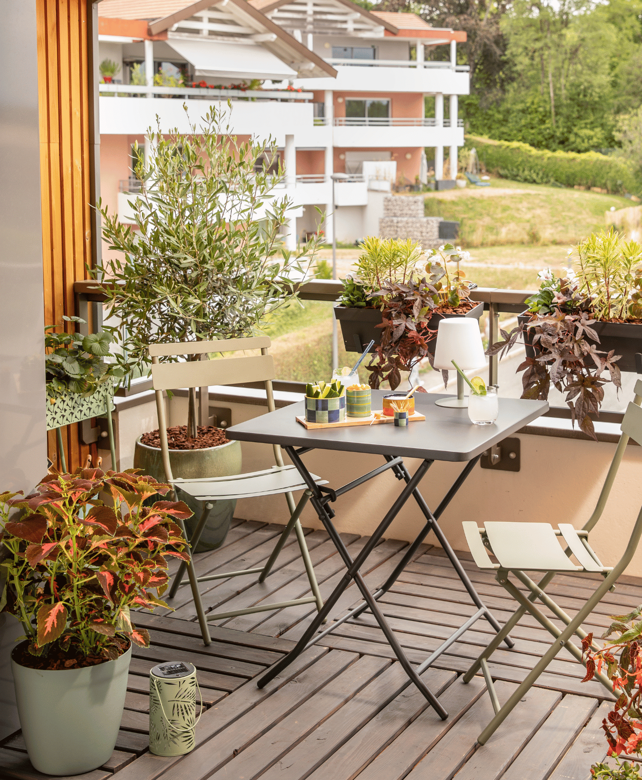 Un balcon urbain aménagé avec des pots, une jardinière, une table et des chaises