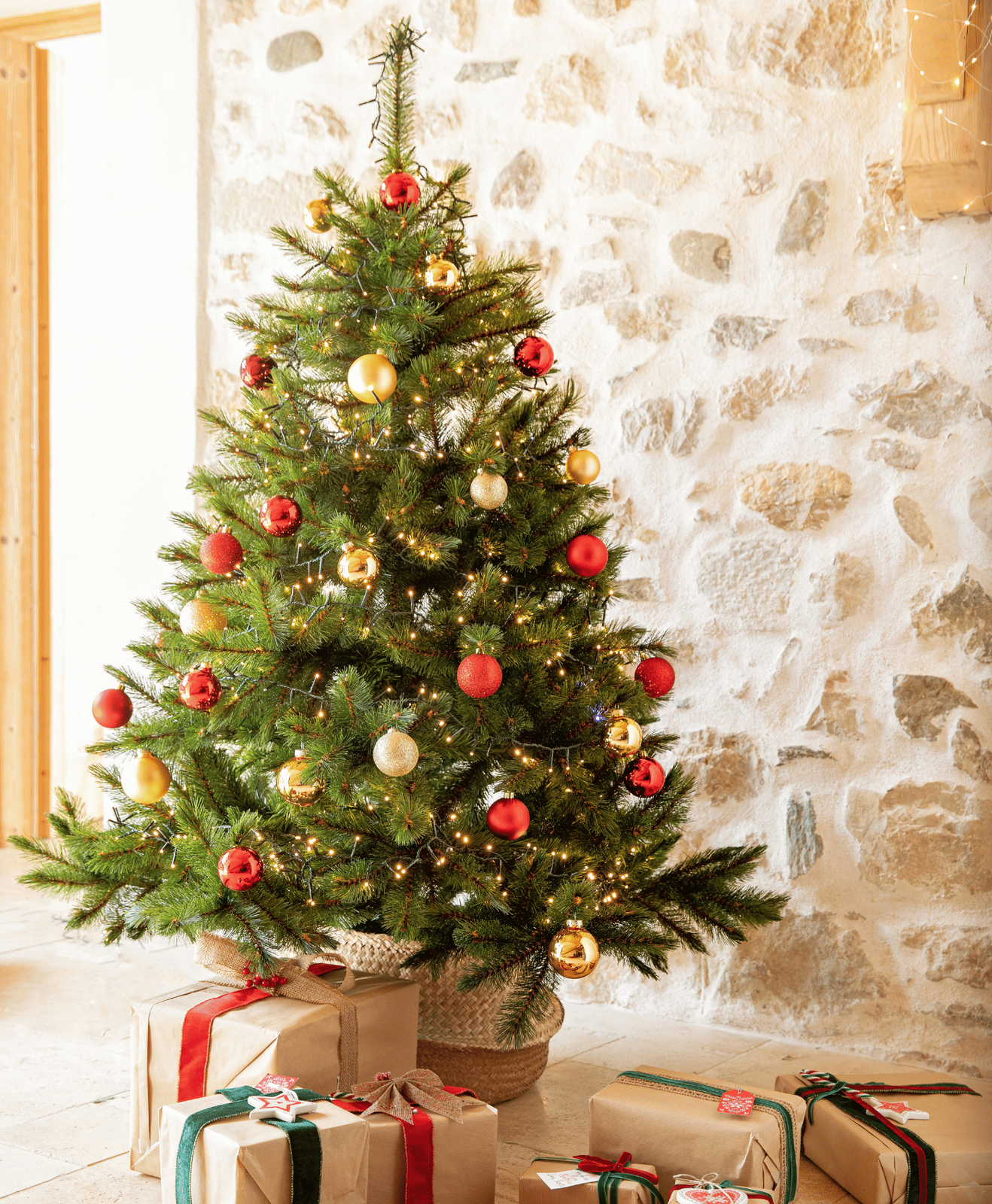 Un sapin artificiel décoré avec des boules de Noël rouges et dorées et une pile de cadeaux à son pied