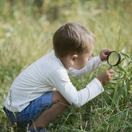 Petit garçon qui explore avec une loupe son jardin