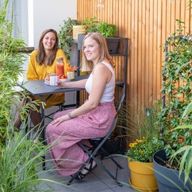 Deux femmes en train de rire sur un balcon végétalisé