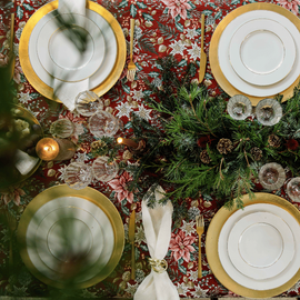 Une table de Noë dressée avec des assiettes dans les tons de bordeaux et or