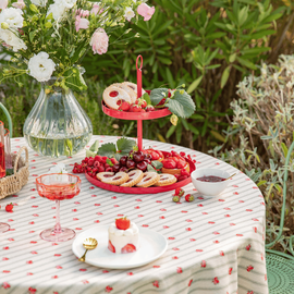 Une table dressée avec une nappe aux motifs fleuris et un présentoir rempli de gourmandises sucrées