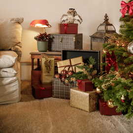 Des cadeaux empilés, deux malles, une lanterne et de la décoration dans un salon entre le sapin de Noël et le canapé