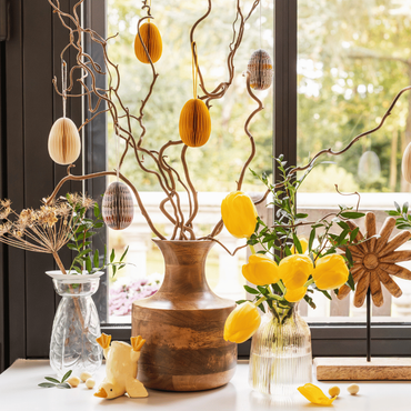 Une décoration de Pâques avec un vase, des branchages et des oeufs déco suspendus