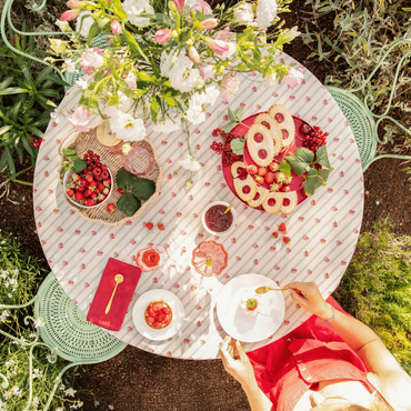 Une décoration de table dans le jardin vue dessus sur laquelle il y a des gourmandises à manger, de la vaisselle et un bouquet de fleurs