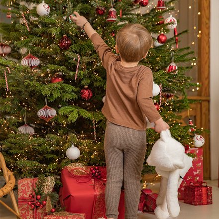 Un enfant de dos qui attrape une boule sur un sapin de Noël
