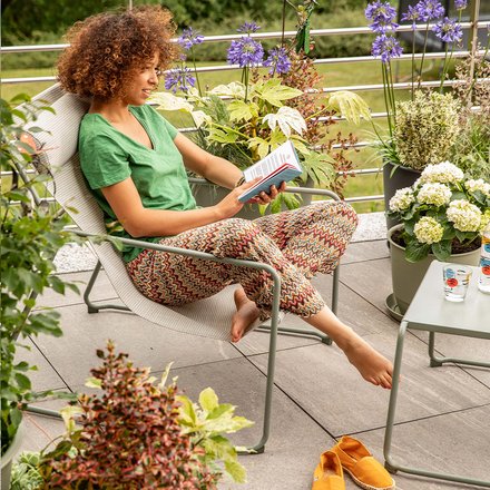 Une femme en train de lire un magazine sur un salon de jardin Oxalis vert kaki