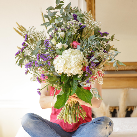 Une femme assise en tailleur tient dans ses mains un bouquet de fleurs.