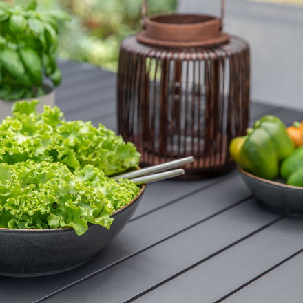 Un bol de salade, une lanterne et un bol de poivrons sur une table de jardin