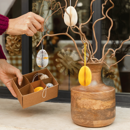 Une femme en train d'installer des oeufs en papier sur des branchages pour Pâques